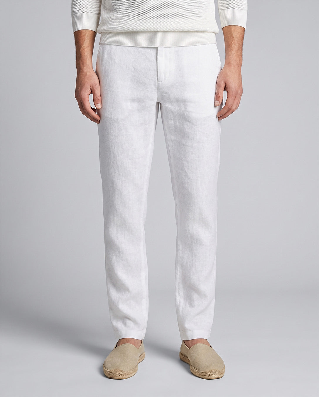 White linen trousers modeled with a cream knit sweater and beige slip-on shoes against a light gray studio background.