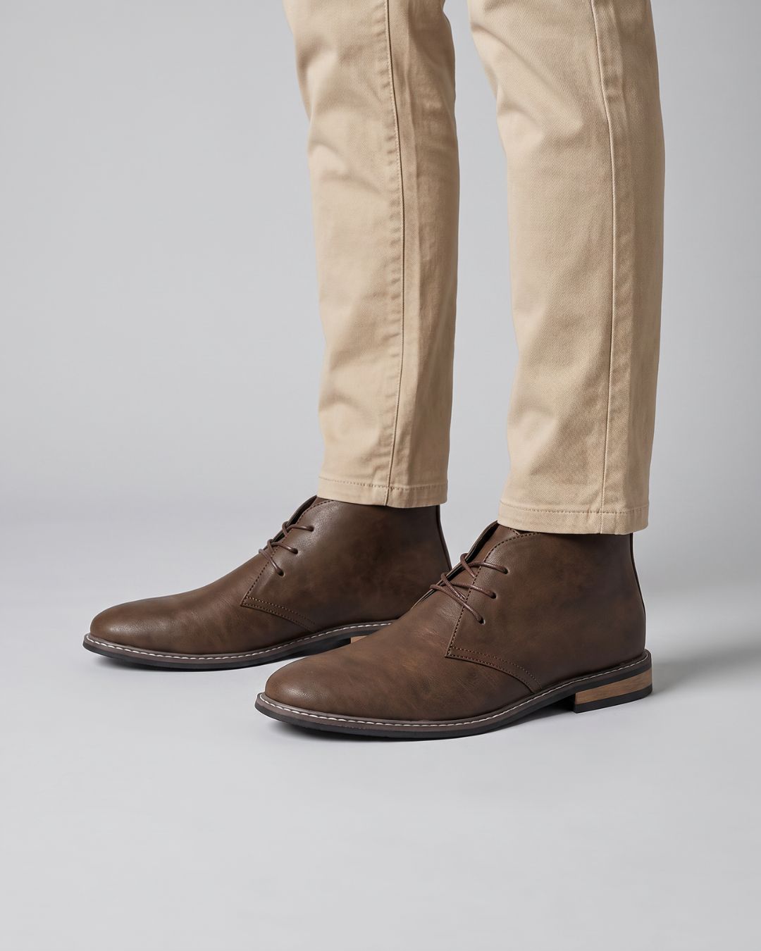A pair of dark brown leather lace-up ankle chukka boots worn with beige trousers, by Hudson & Tate.
