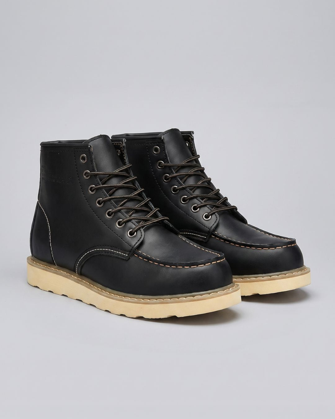 A pair of black leather lace-up ankle boots with contrast stitching and thick beige soles, photographed on a light gray studio background.