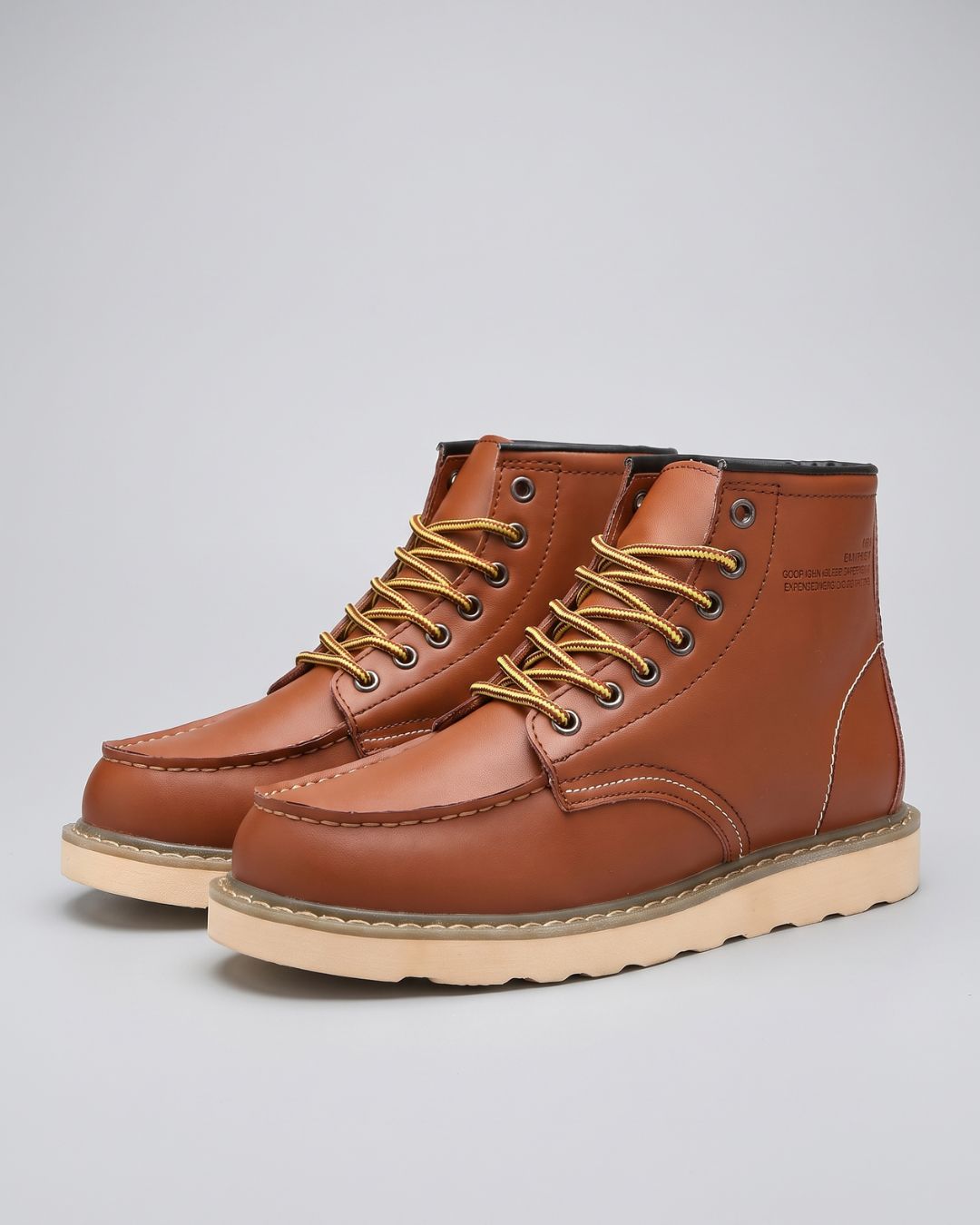 A pair of men's cognac leather lace-up boots with tan laces and a light beige sole, photographed on a neutral light gray background.
