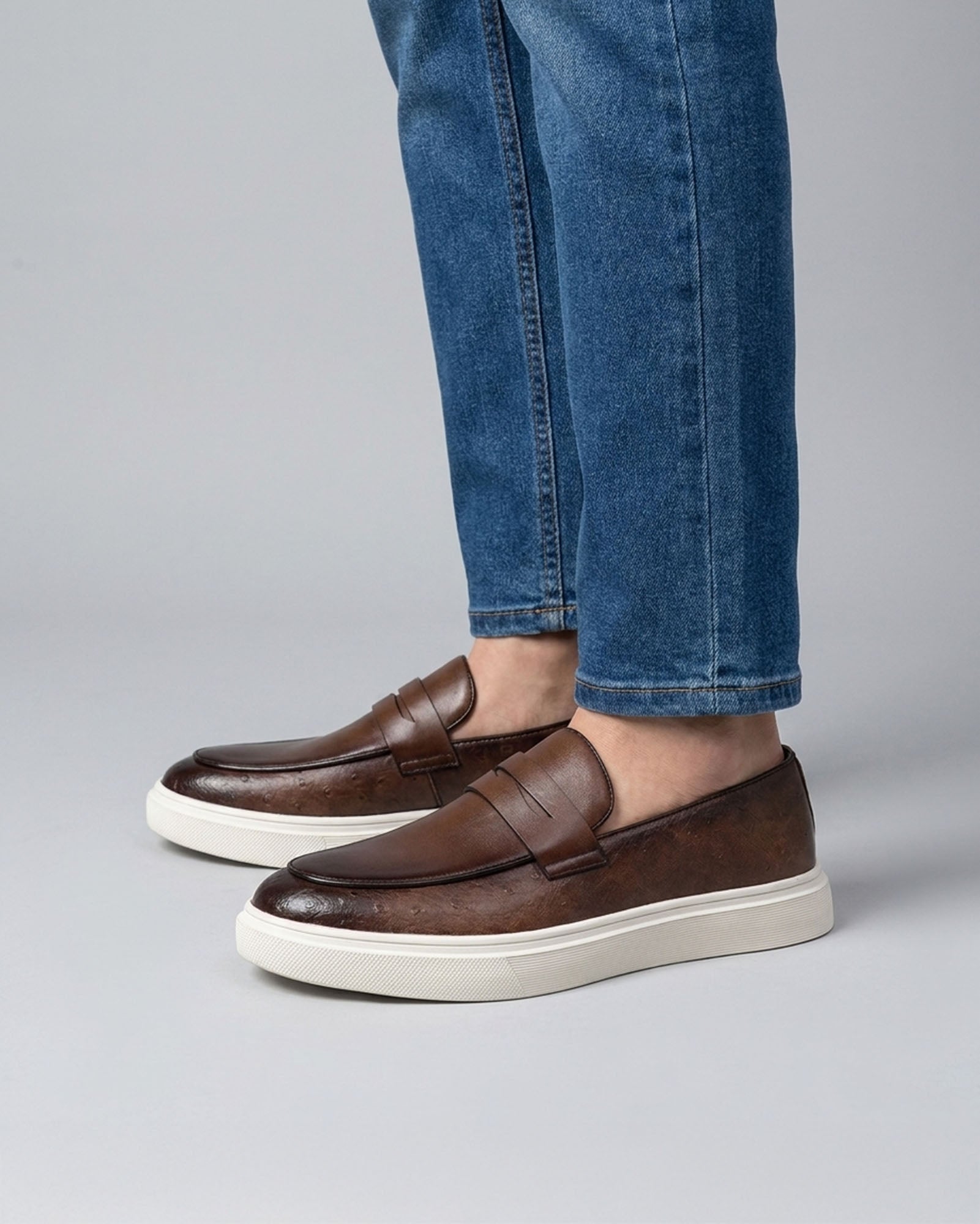 Belmont men's brown penny loafer sneakers styled with blue denim jeans on grey background