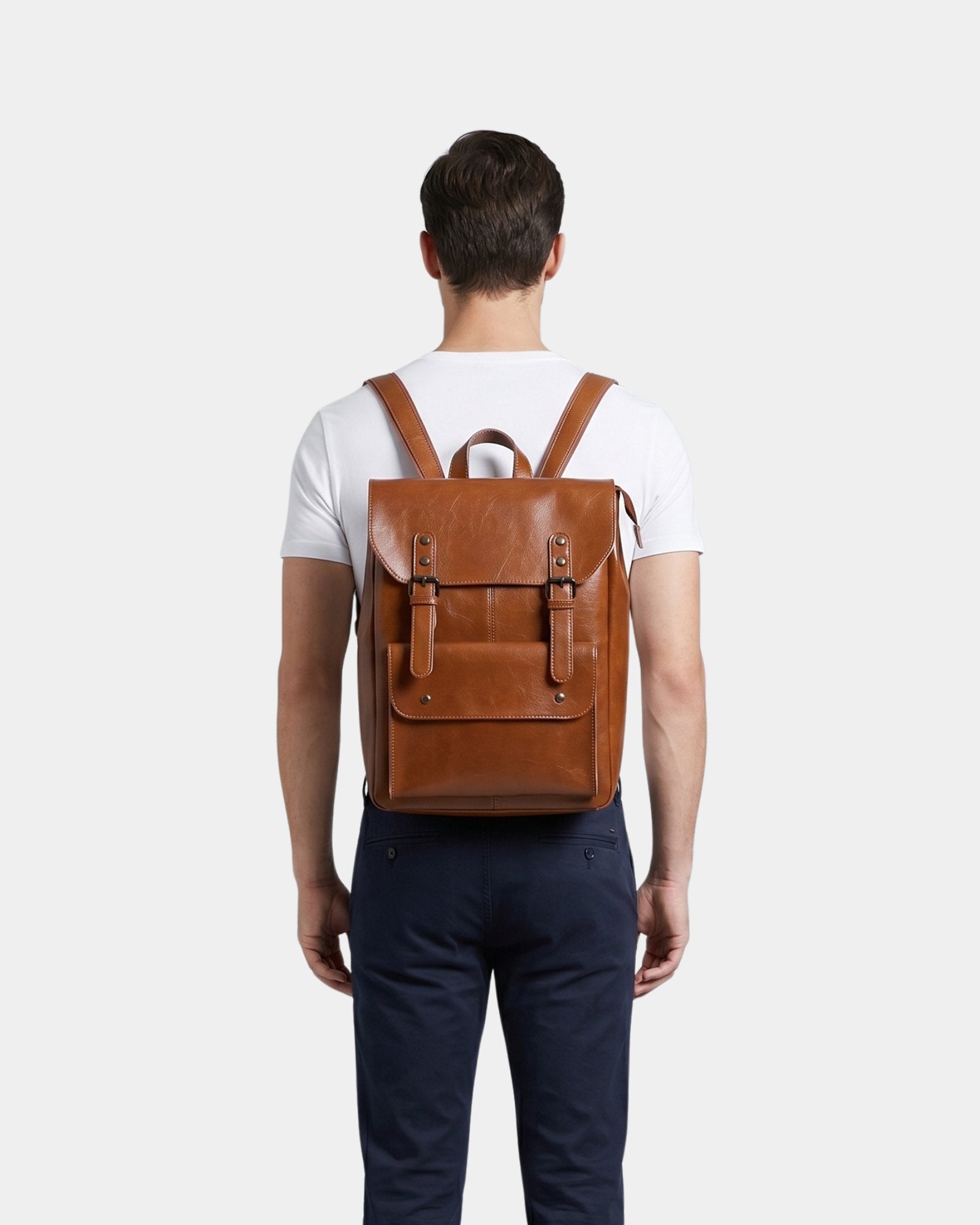 Cambridge brown leather backpack worn on the back styled with white t-shirt and navy trousers