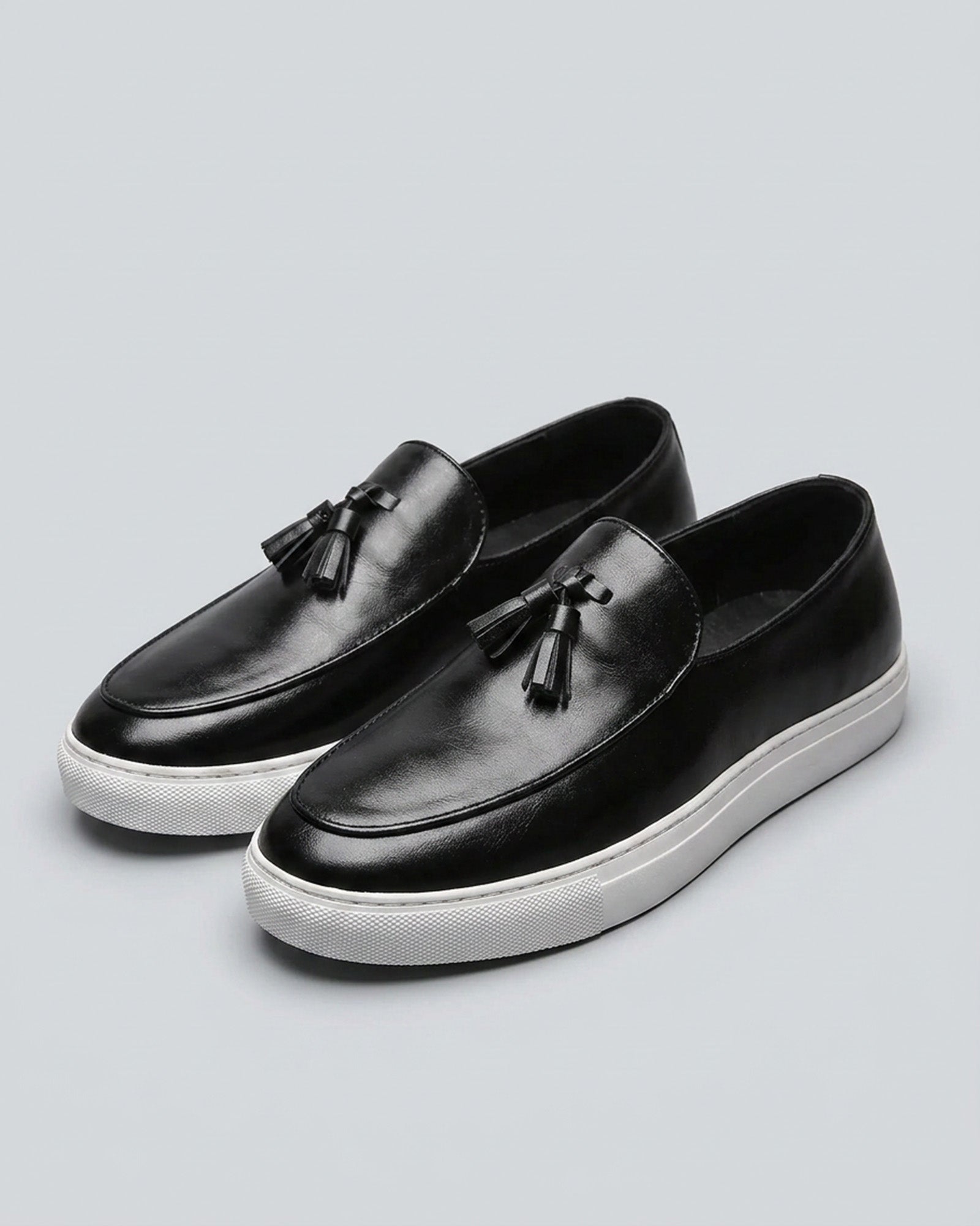 Pair of Capri men's black leather tassel loafers with white cupsole on grey background