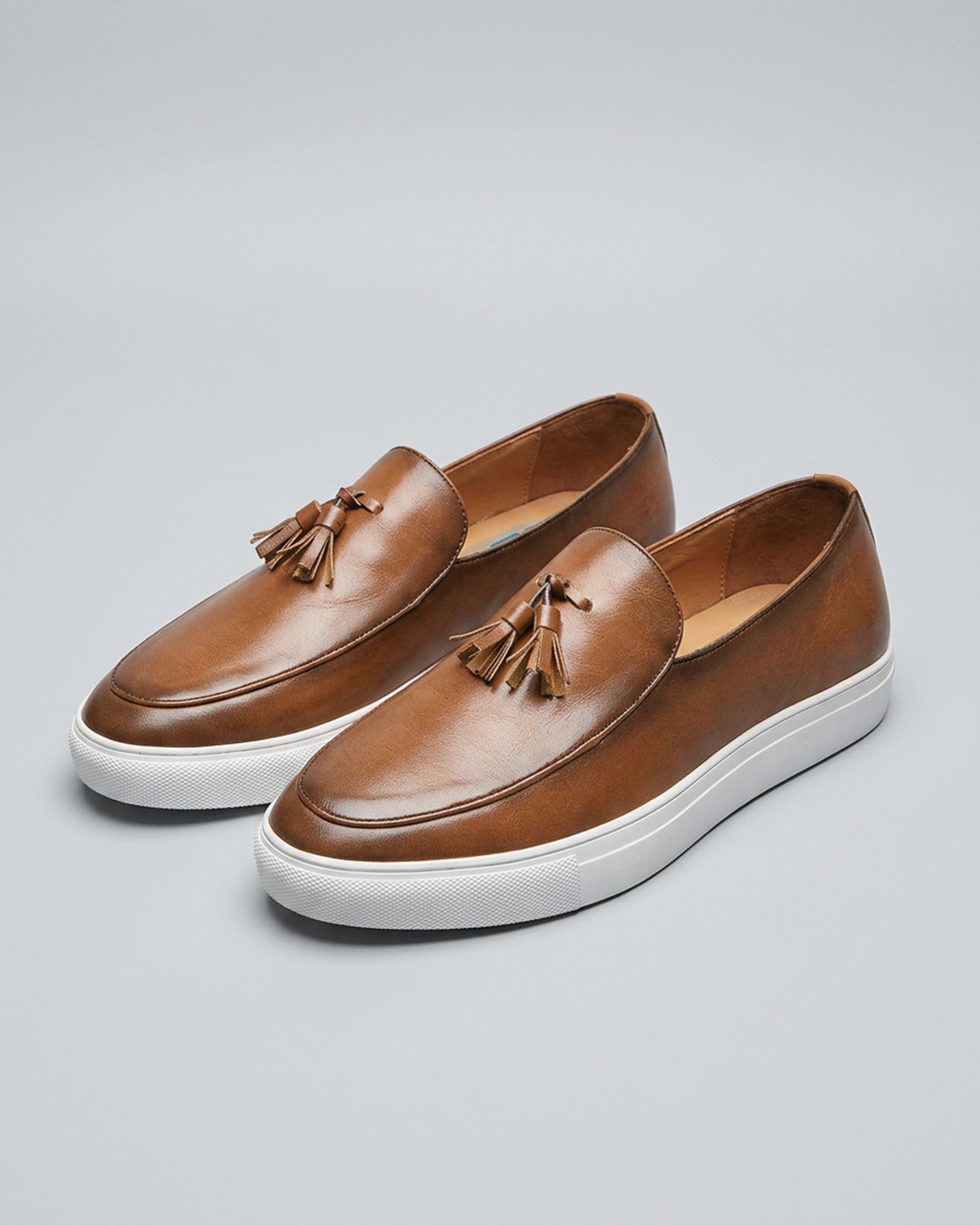 Pair of Capri men's cognac leather tassel loafers with white cupsole on grey background