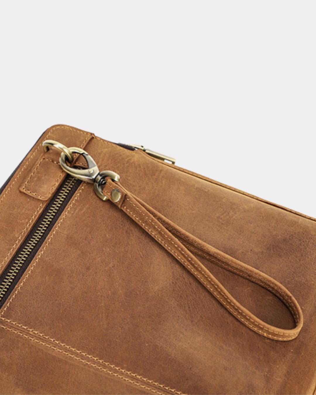 Close-up of a brown leather laptop sleeve with a wrist strap and metal zipper hardware on a light gray background.