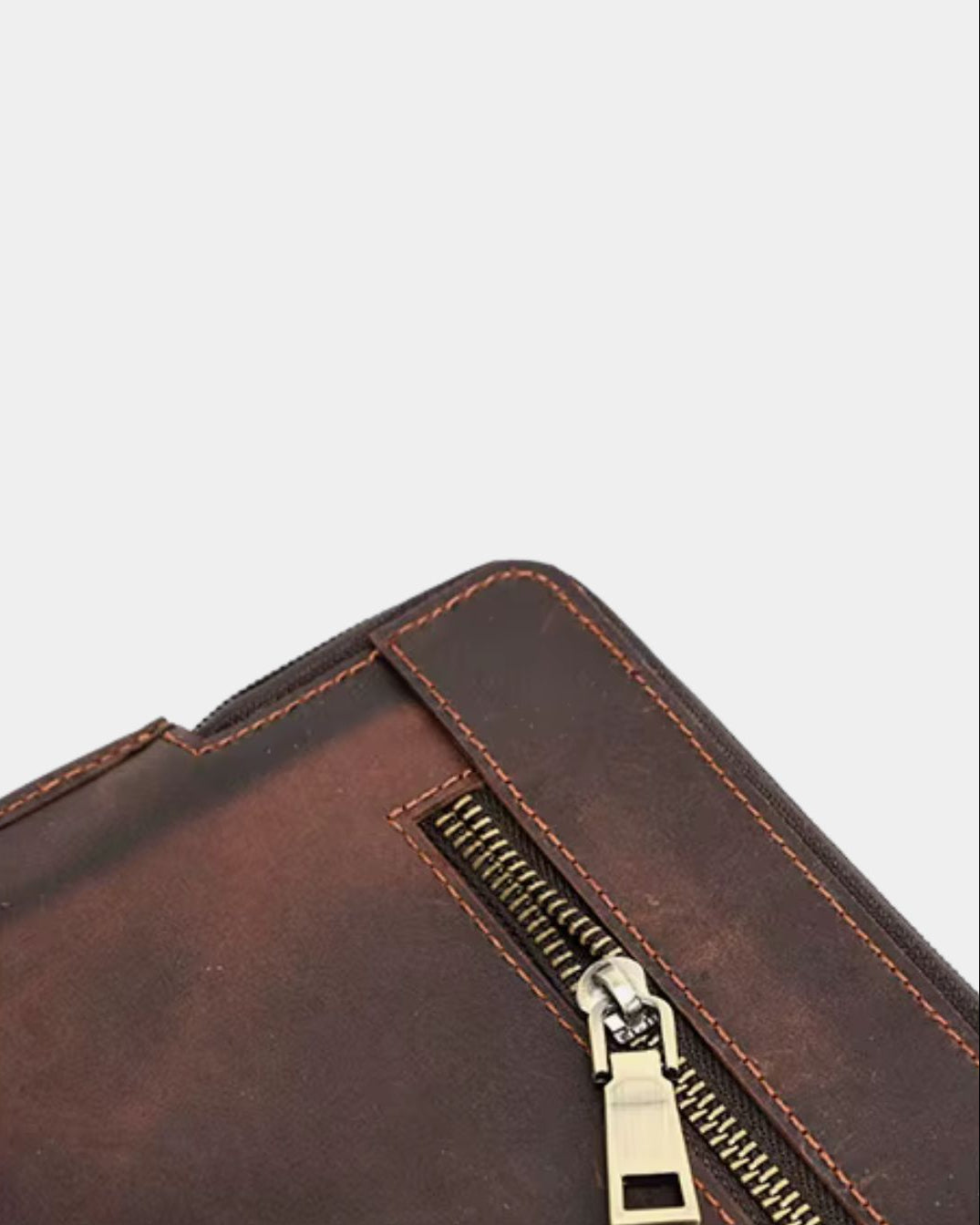Close-up of a dark brown leather zippered laptop sleeve with visible stitching and a brass-toned zipper pull on a light gray background.