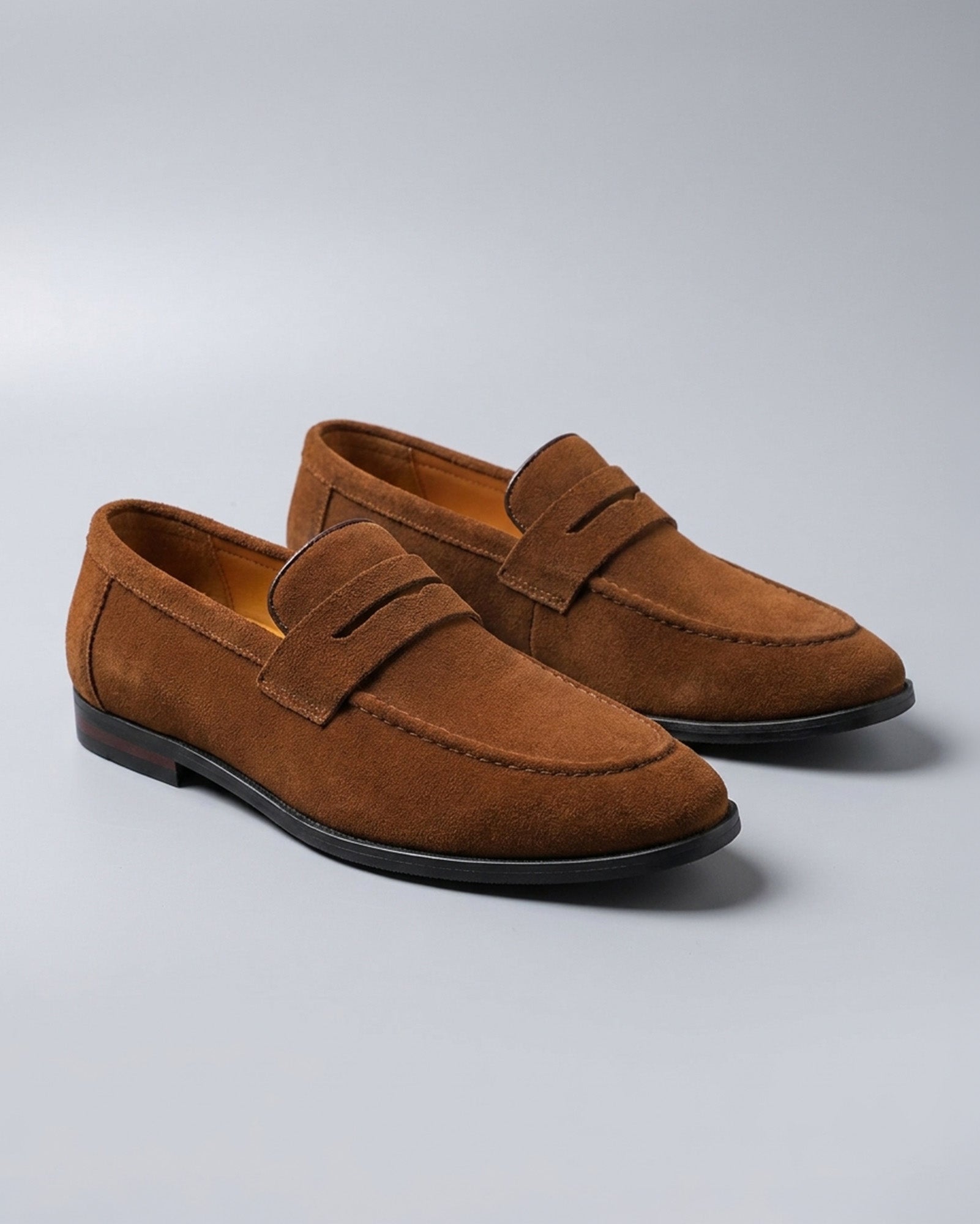 Pair of Harper men's cognac suede penny loafers on grey background