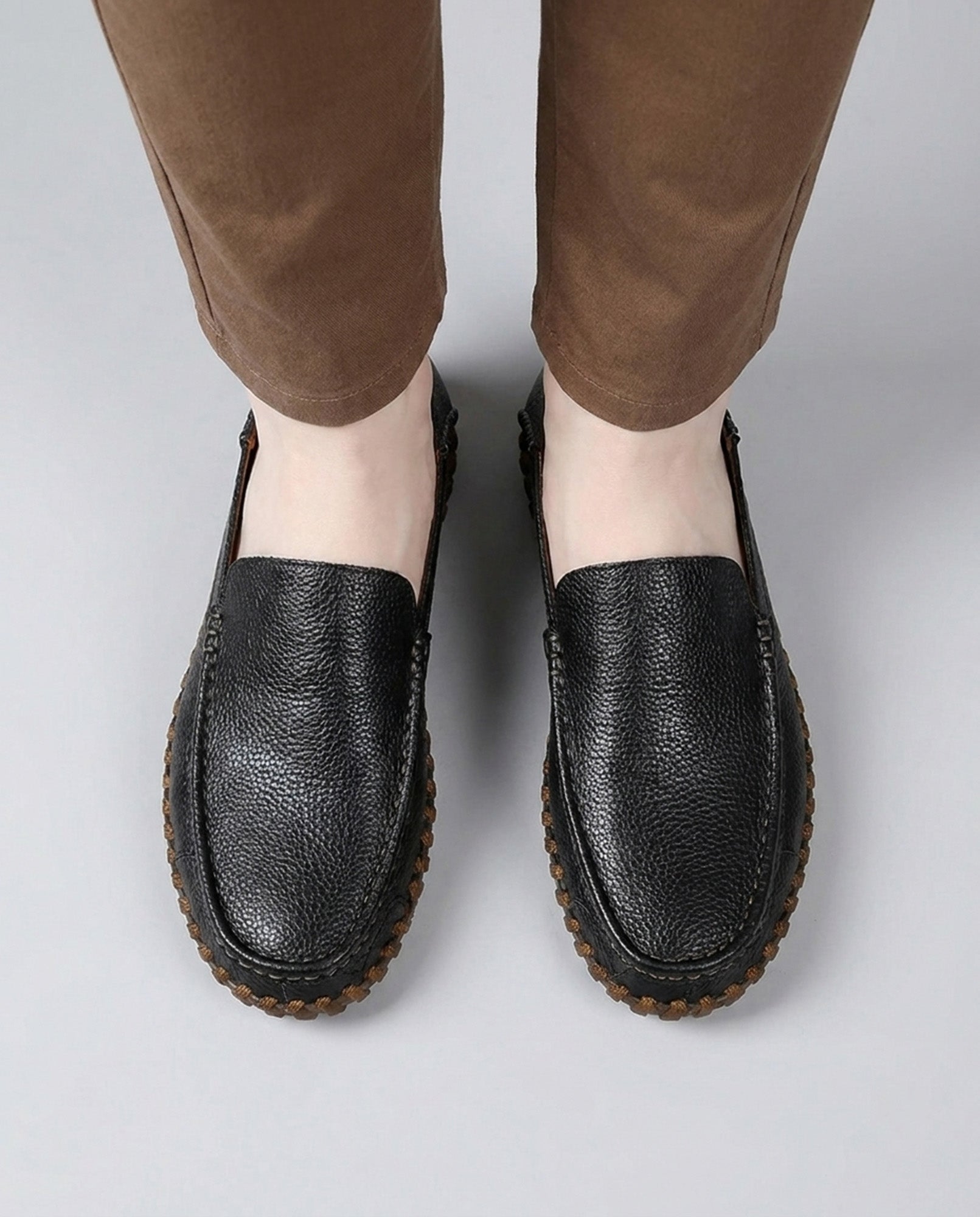Overhead view of Marlow men's black leather driving loafers worn with tan chinos