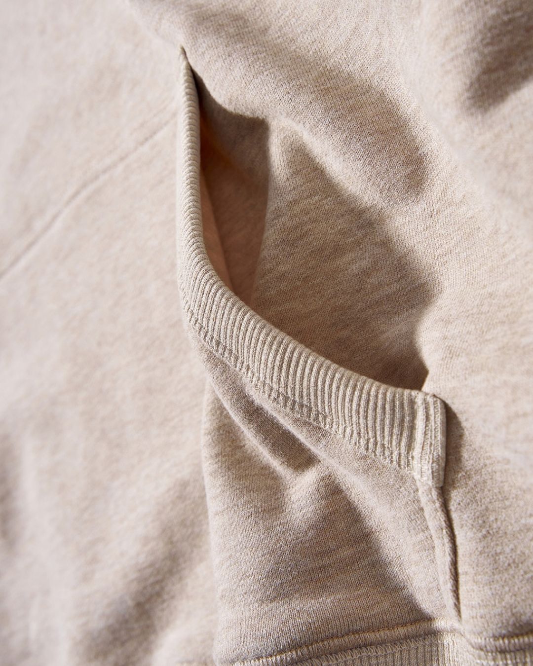 Close-up of a beige oversized cotton hoodie featuring a ribbed kangaroo pocket and soft, thick fabric texture.