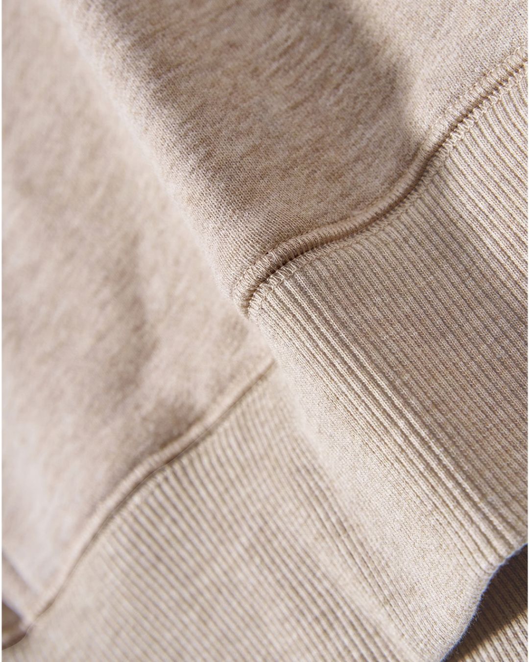 Close-up of a beige oversized cotton hoodie showing the soft fabric texture and ribbed hem detail.