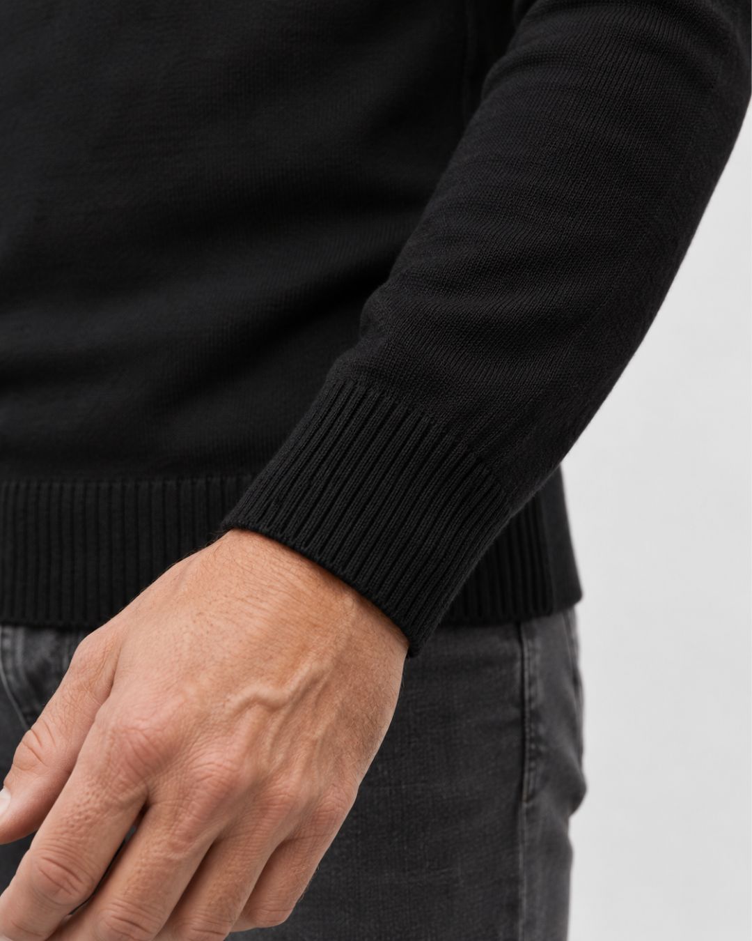 Close-up of a men's black knit turtleneck sweater featuring a ribbed cuff and soft, warm fleece-lined interior.