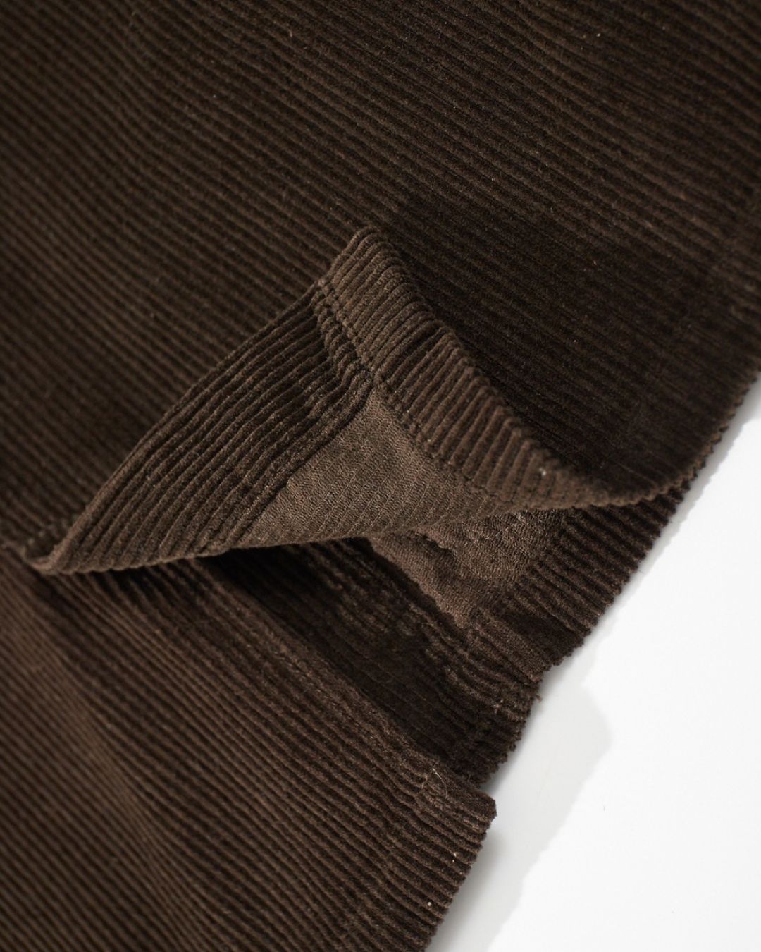 Close-up of soft brown ribbed cotton corduroy fabric with a folded edge showing texture and stitching.