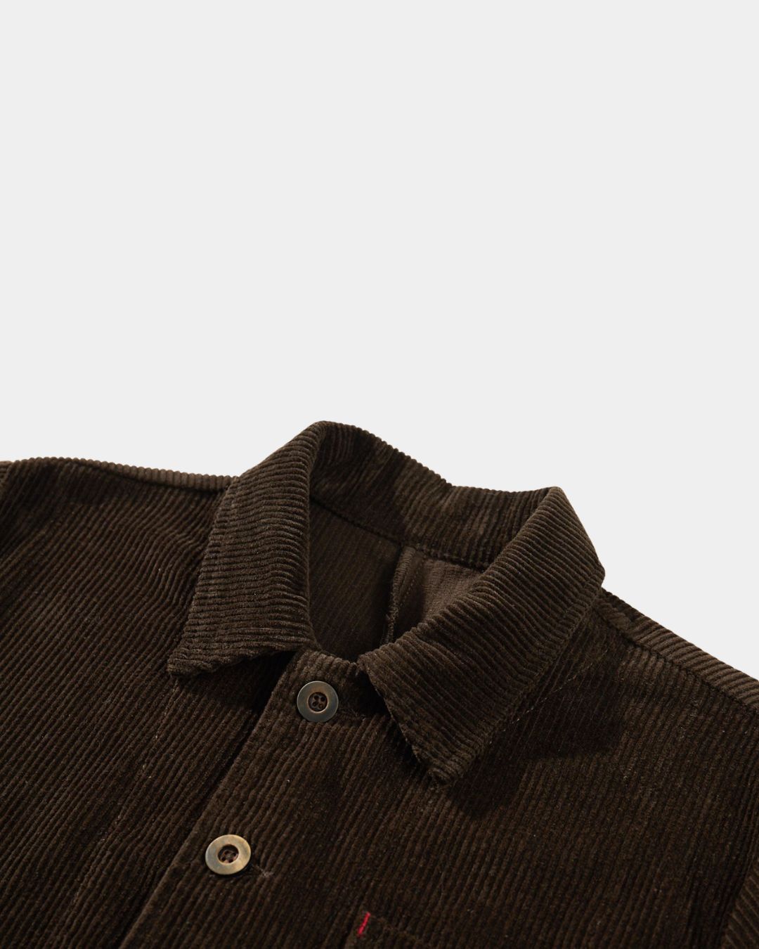 Brown corduroy chore jacket with a point collar, button front, and subtle red bar-tack stitching detail.
