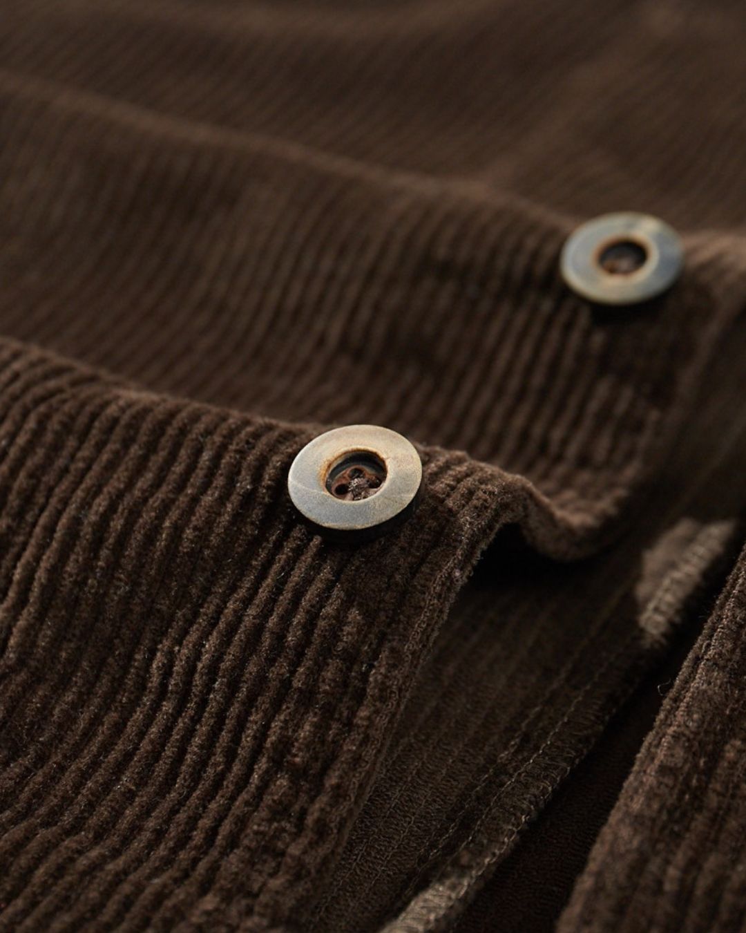Close-up of a brown cotton corduroy chore jacket featuring textured ribbed fabric and dark button closures.