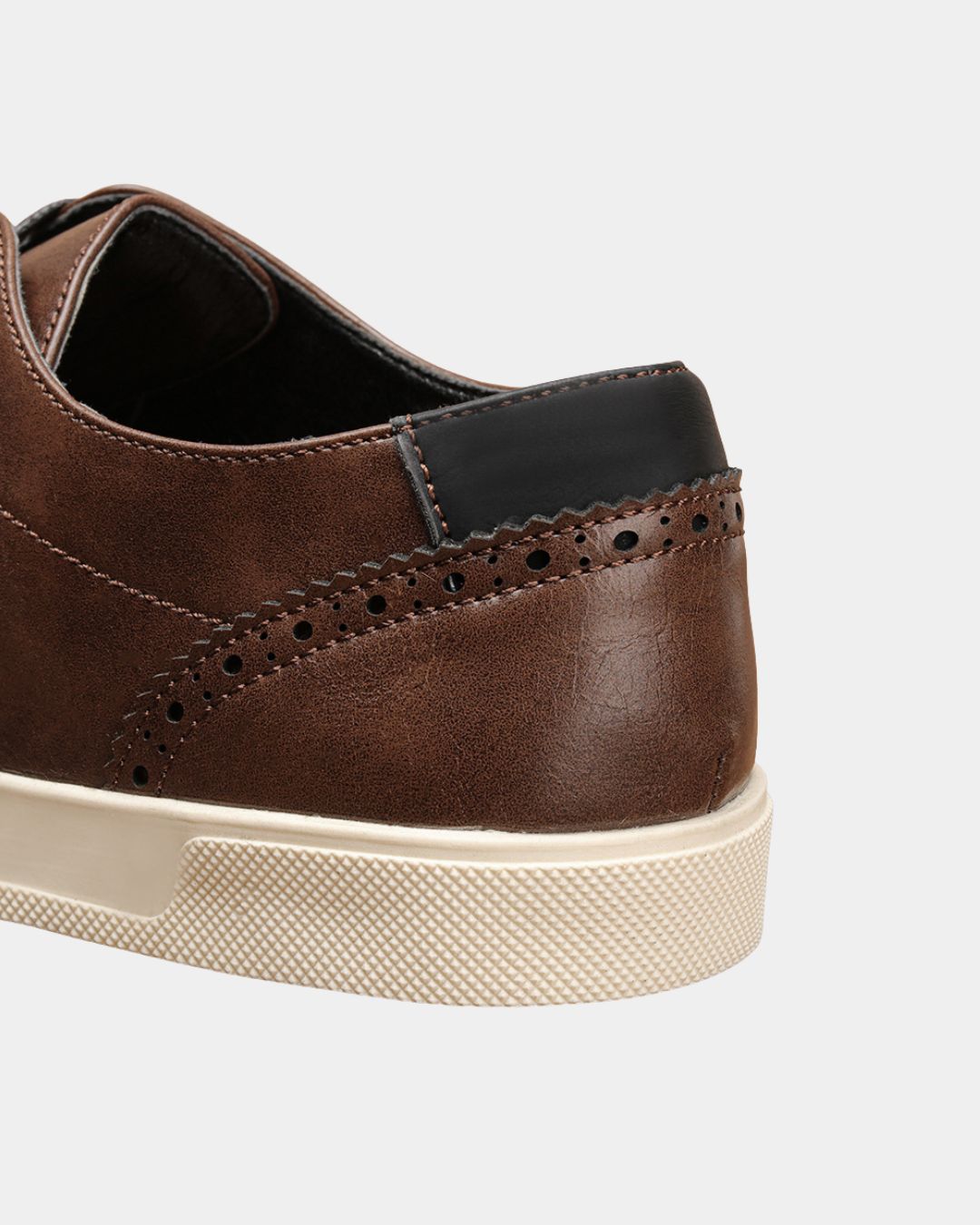 Brown faux leather dress sneaker with heel brogue detailing, black contrast tab, and a textured cream rubber sole.