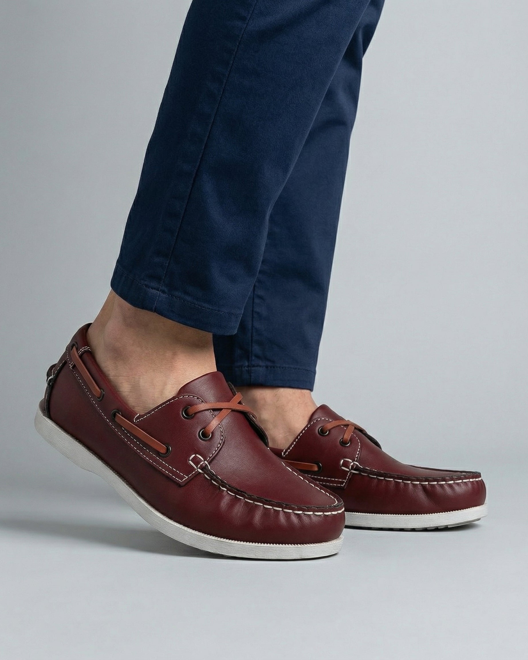 Men's burgundy lace-up boat shoes with tan trim and white sole worn with navy chino trousers – close up