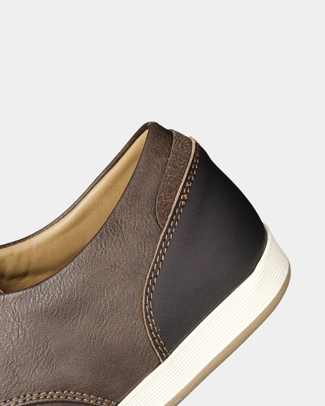 Close-up of a brown synthetic leather casual dress sneaker with contrast stitching and a white rubber sole.