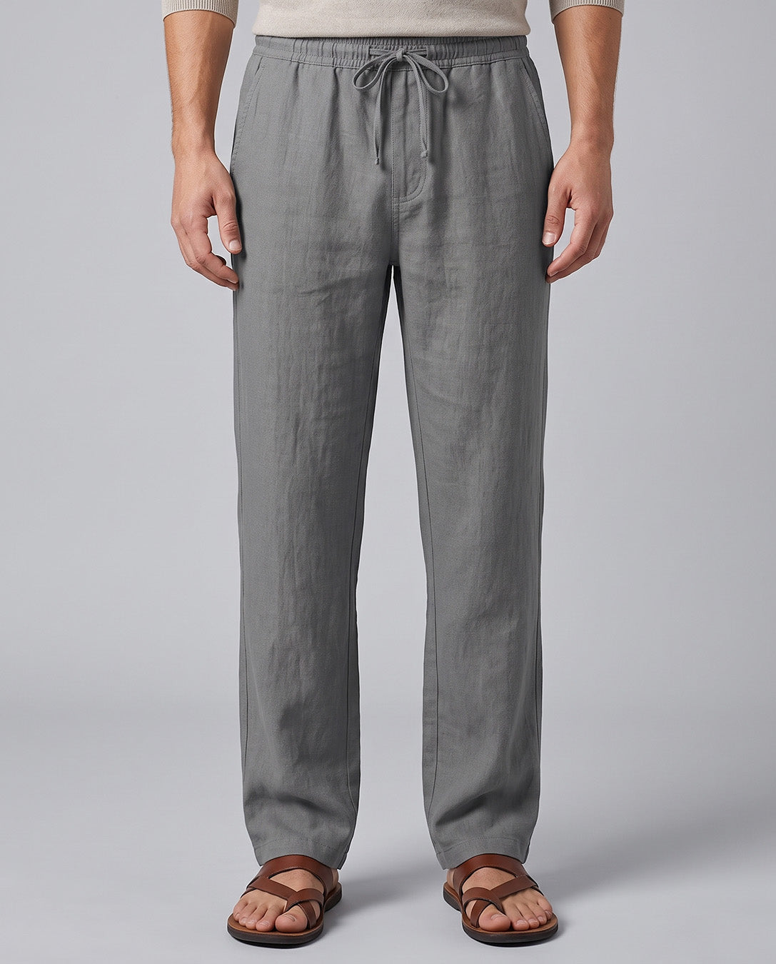 A person wearing light gray drawstring pants and brown sandals, shown from the waist down against a plain light gray studio background.
