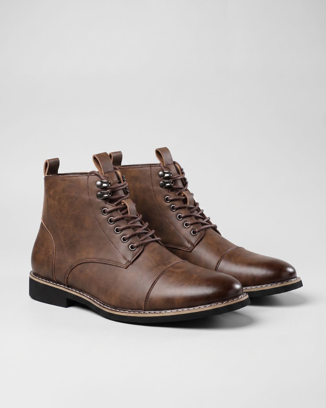 Brown leather cap-toe ankle boots with lace-up front, metal eyelets, and side zippers on a light grey background.