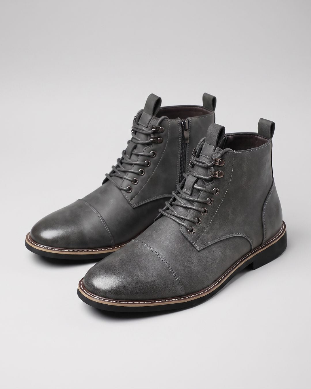 Grey men’s cap-toe ankle boots with lace-up front, metal eyelets, and convenient side zippers on a light background.