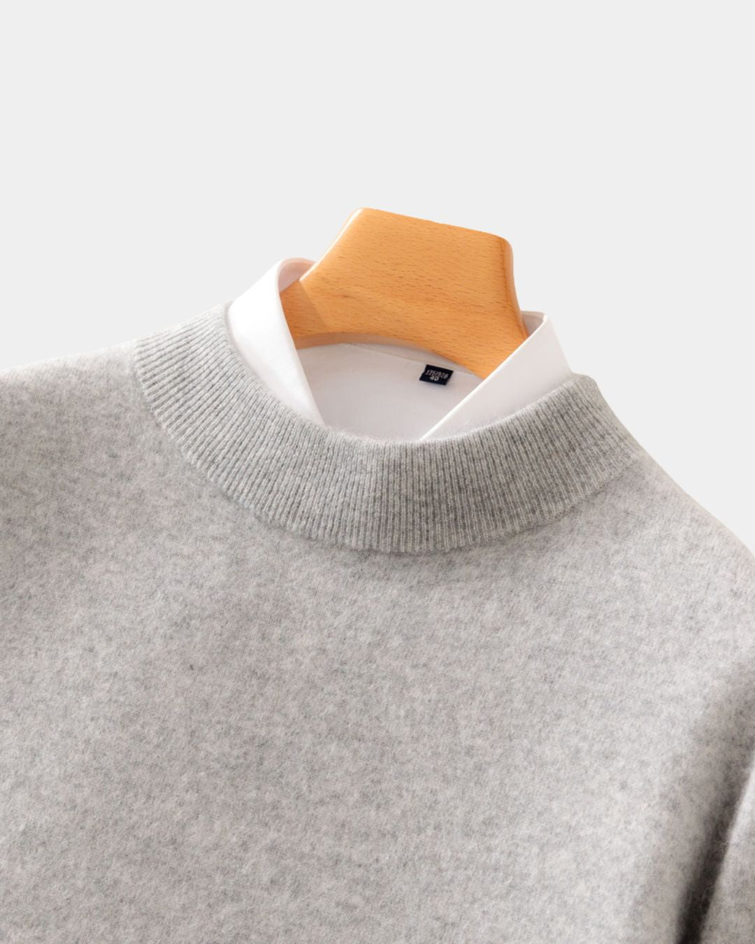 Grey wool mock neck sweater layered over a white collared shirt on a wooden hanger.