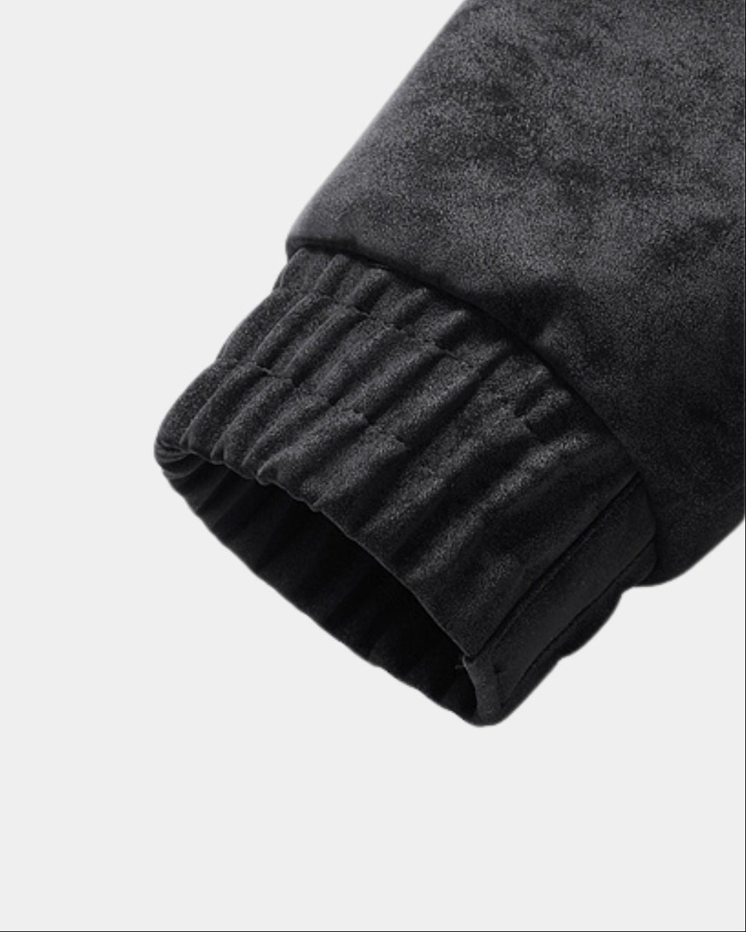 Close-up of a black cuff of a black bomber jacket, shown against a light gray background.