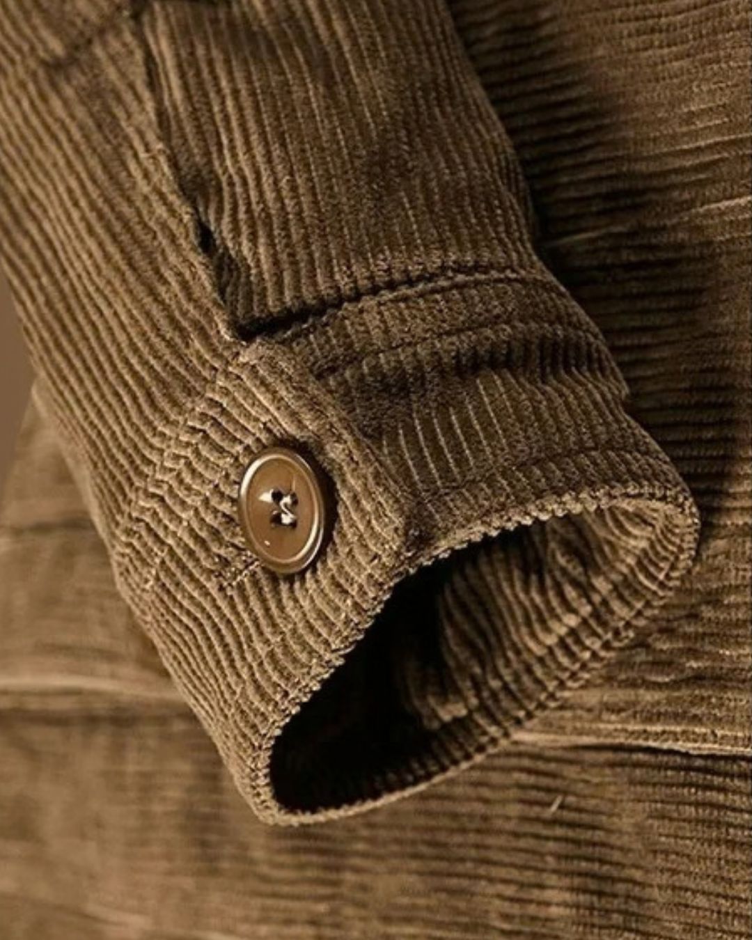 Close-up of a brown corduroy trucker jacket sleeve featuring a buttoned cuff and textured fabric detail.