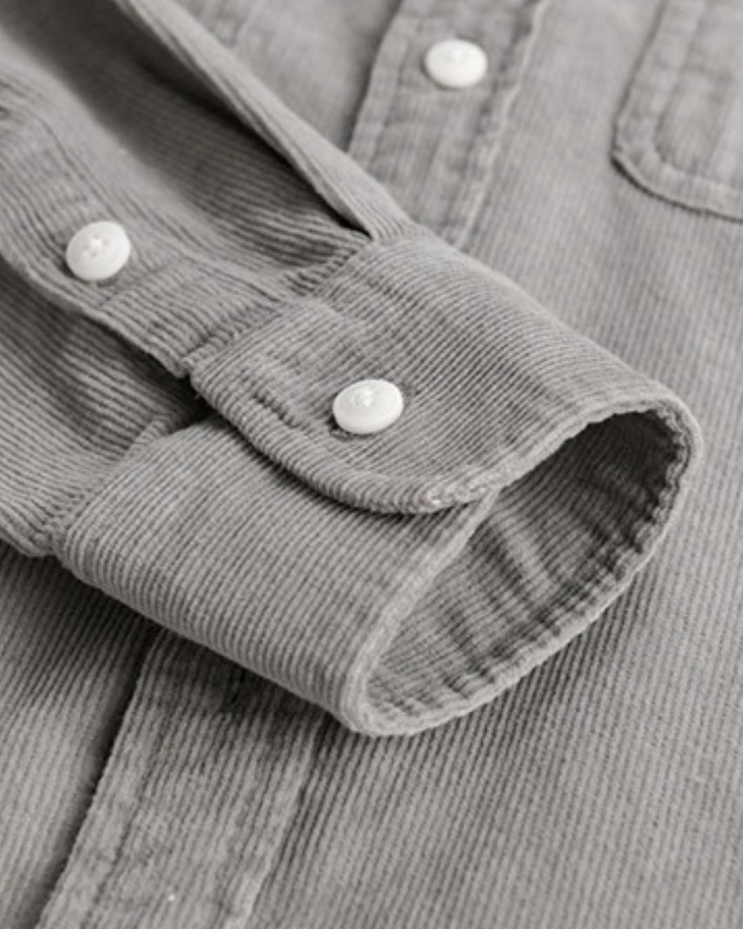 Close-up of a grey cotton corduroy button-up shirt featuring a ribbed texture, long sleeves, and white buttons.