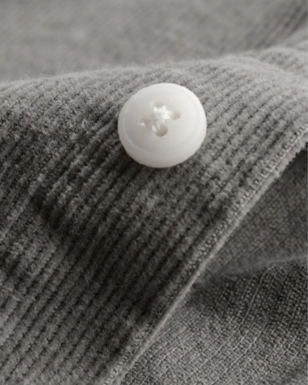 Close-up of a grey cotton corduroy shirt featuring a soft ribbed texture and a single white button.