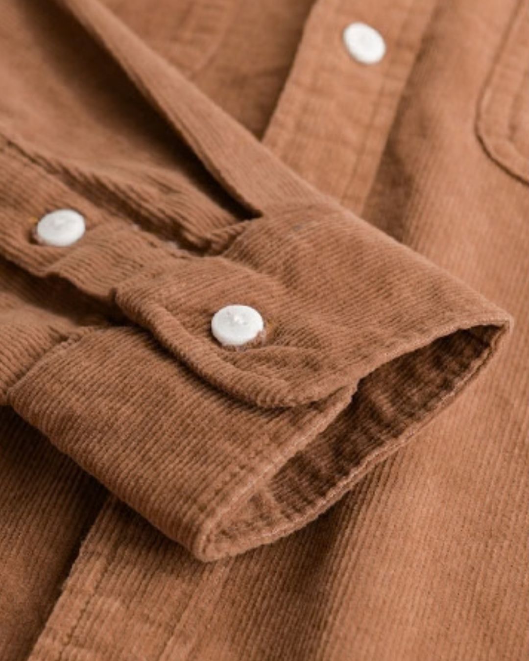 Close-up of a brown cotton corduroy shirt featuring ribbed texture, long sleeves, and white button cuffs.