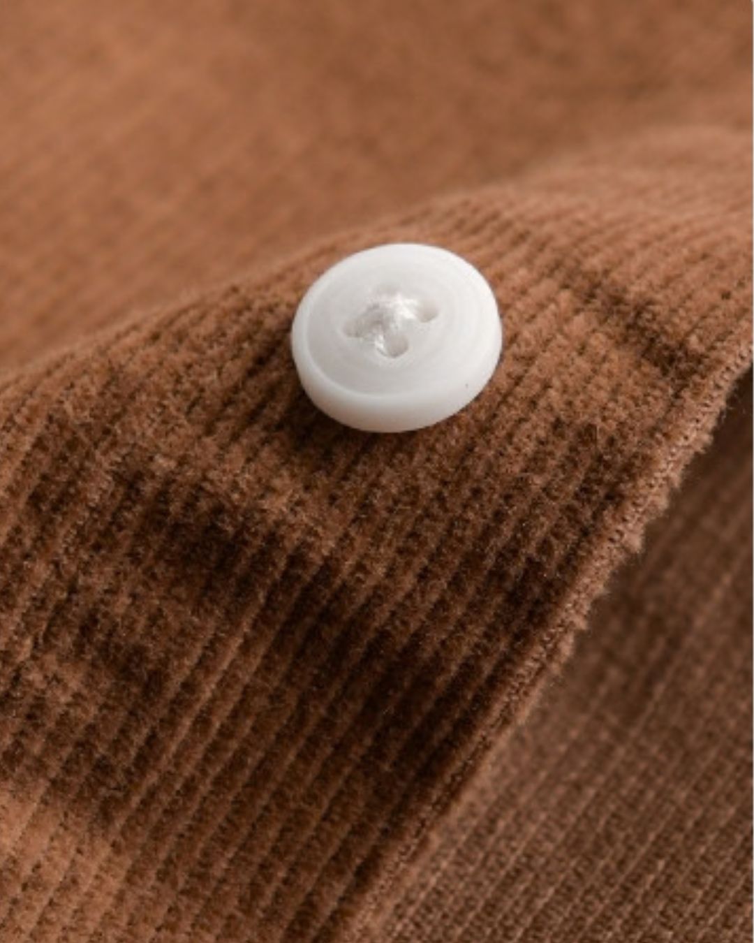 Close-up of brown cotton corduroy fabric with a white button detail.