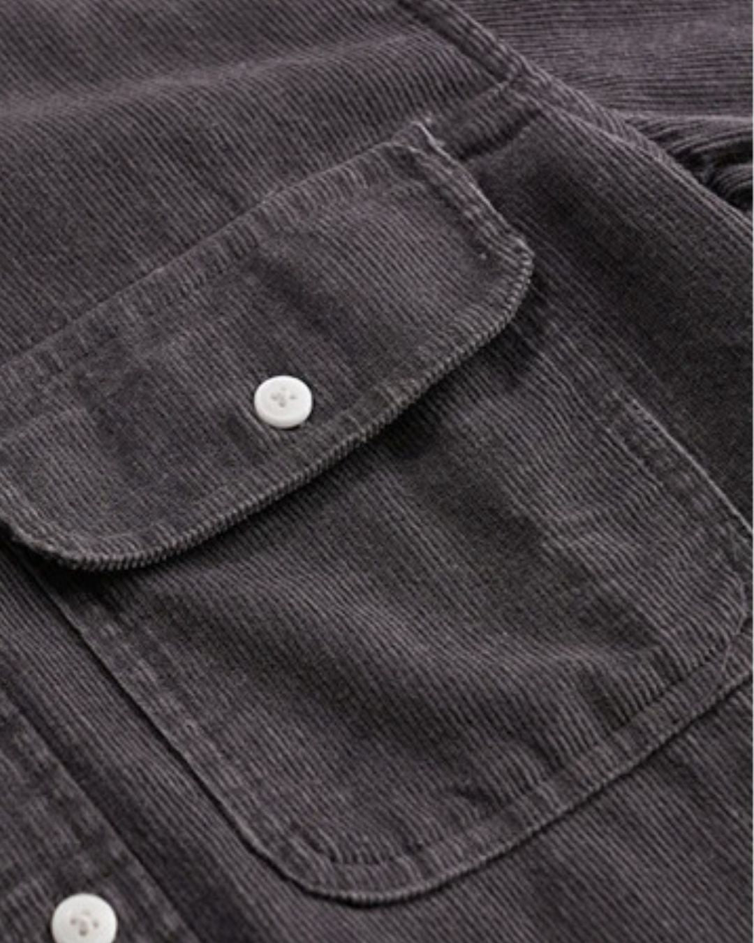 Close-up of a charcoal grey cotton corduroy shirt featuring a button-flap chest pocket and white buttons.