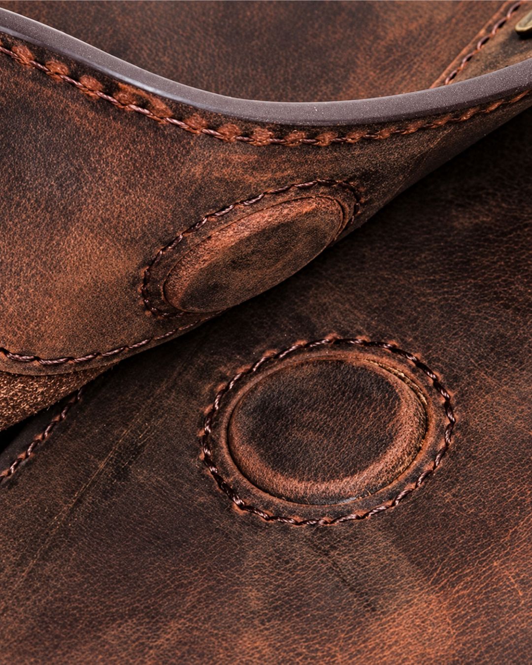 Close-up of brown distressed Crazy Horse leather with visible stitching and circular magnetic snap closure details.