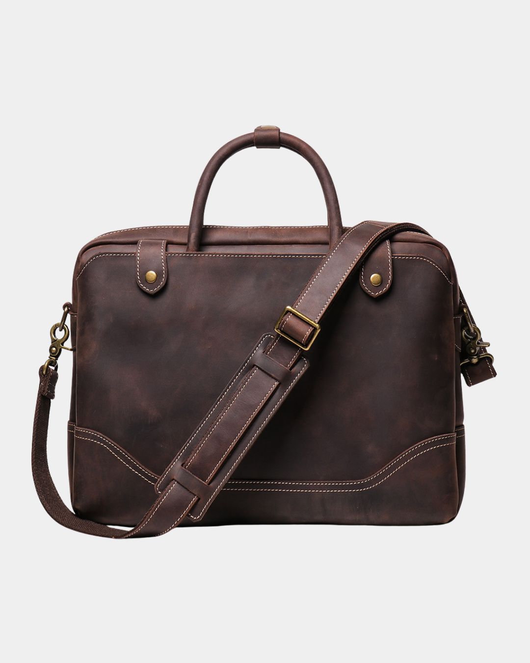 A dark brown distressed leather briefcase with a top handle, adjustable shoulder strap, brass hardware, and contrast stitching, shown against a light gray background.