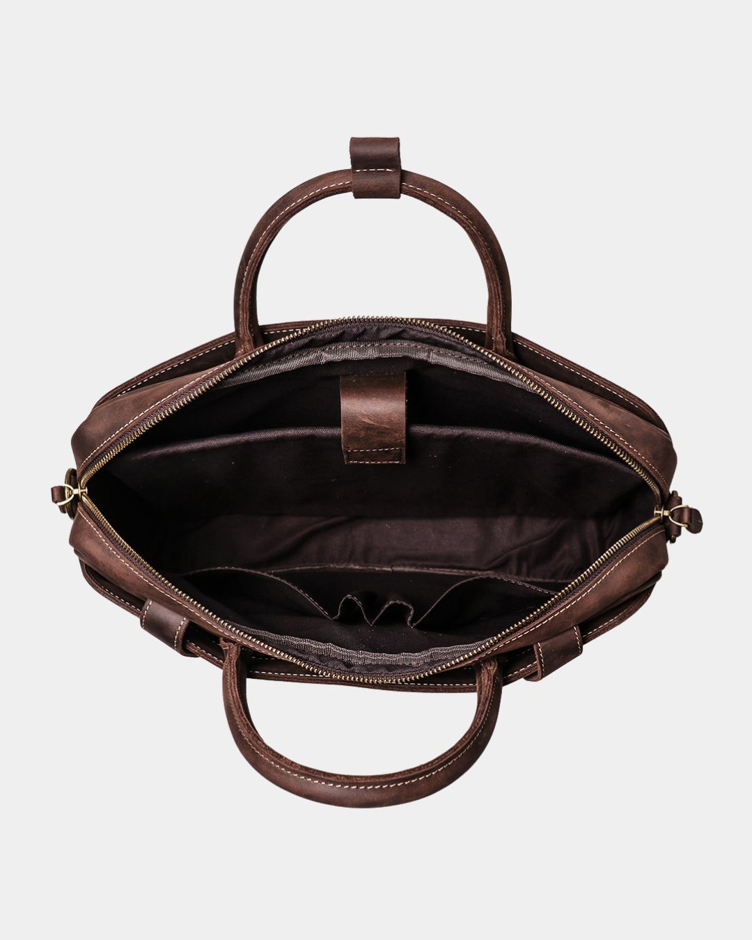 An overhead view of a dark brown leather handbag's open interior, showing the deep lining, zippered compartments, and top handles against a light gray background.