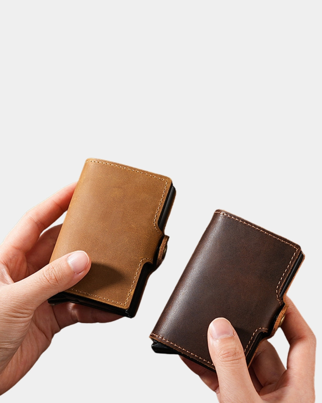Two compact genuine cowhide leather pop-up card wallets in light and dark brown held in hands.