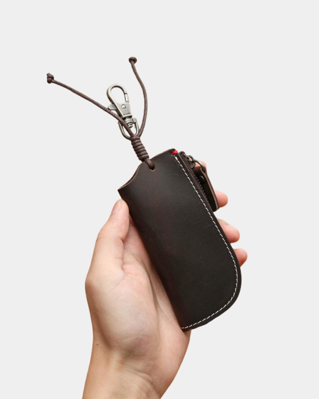 Handheld dark brown genuine cowhide leather key wallet with a metal clip, zipper closure, and white contrast stitching.