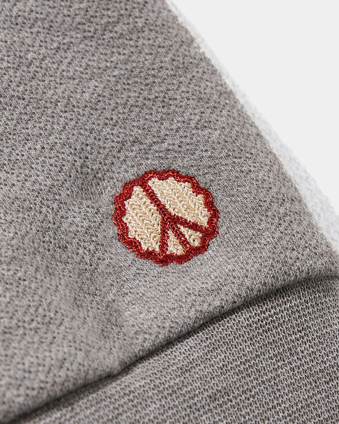 Close-up of gray heavyweight cotton knit fabric featuring a small, embroidered red and beige peace symbol on the cuff.