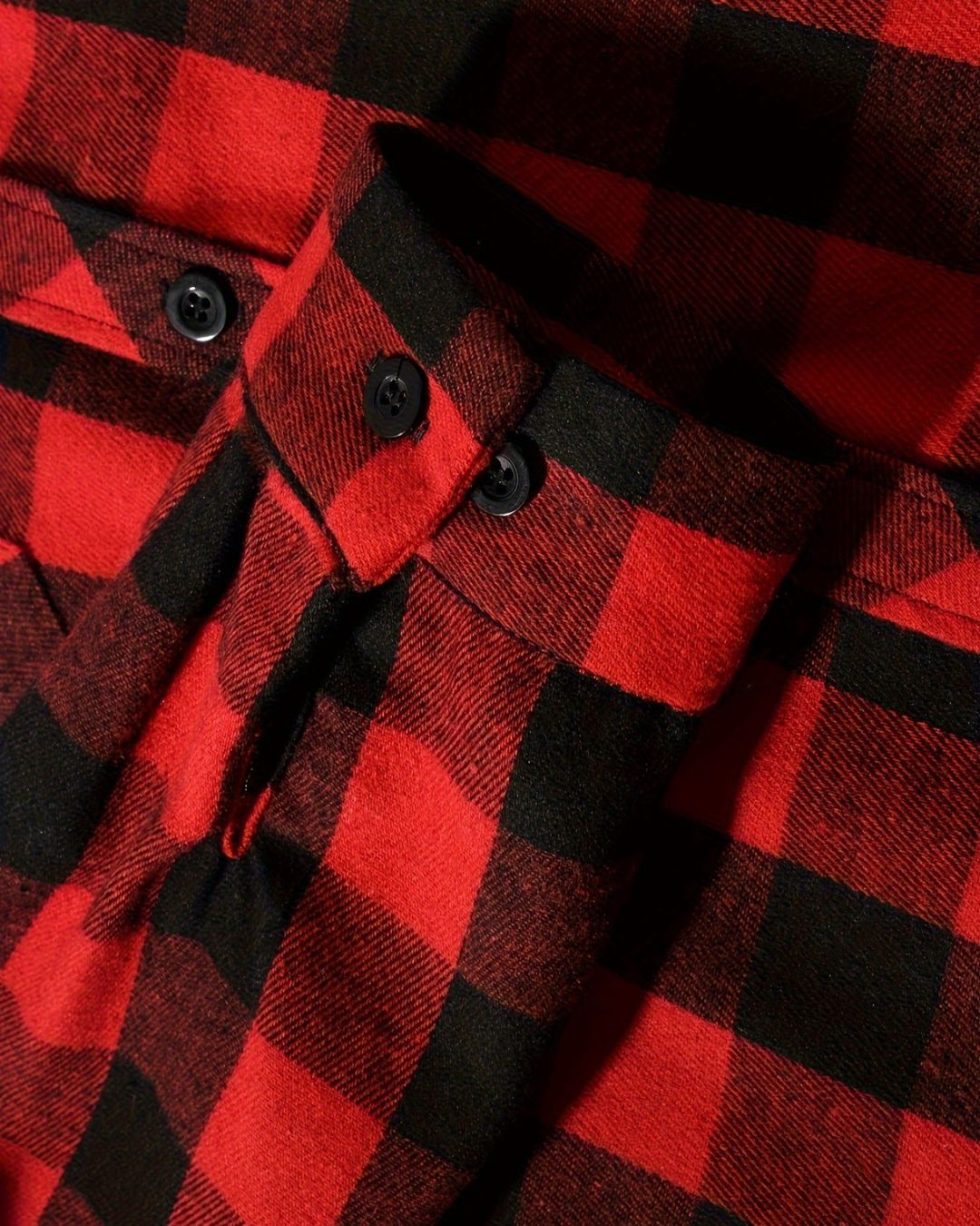 Close-up of a red and black plaid brushed flannel shirt featuring buttoned cuffs and a soft textured fabric.