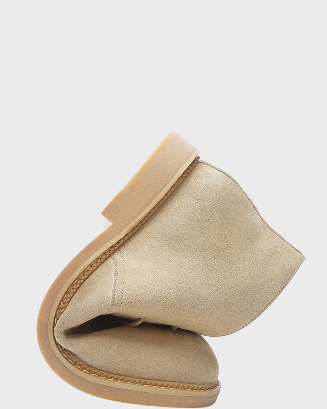 A pair of beige suede chukka boots with a braided trim detail along the edge.