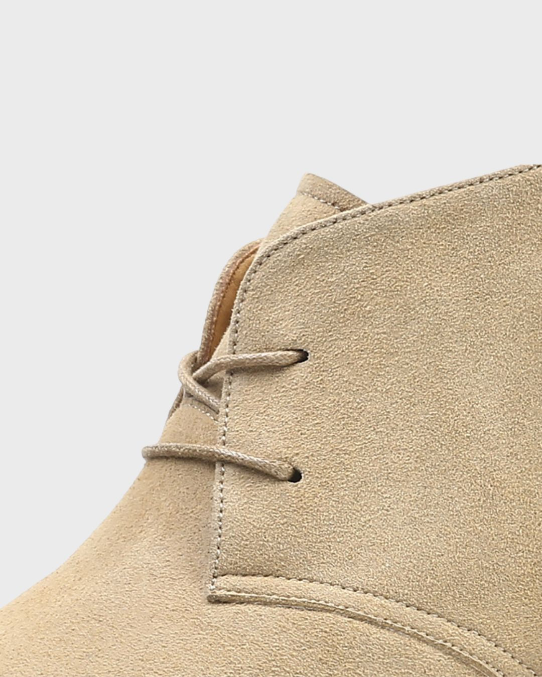 Close-up of a beige suede chukka boot showing the lace-up front and stitching.