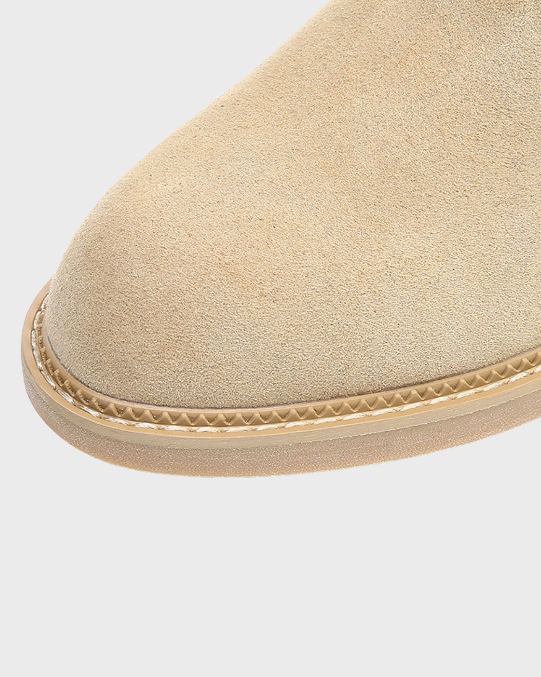 Close-up of a beige suede chukka boot toe with a textured sole and decorative stitching