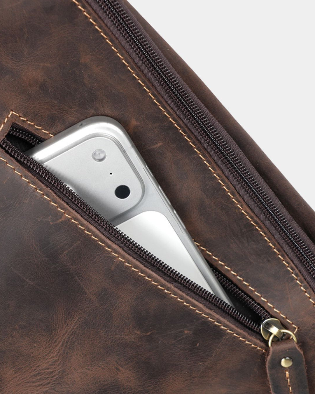 Dark brown vintage leather crossbody sling bag with a secure zippered pocket holding a smartphone.