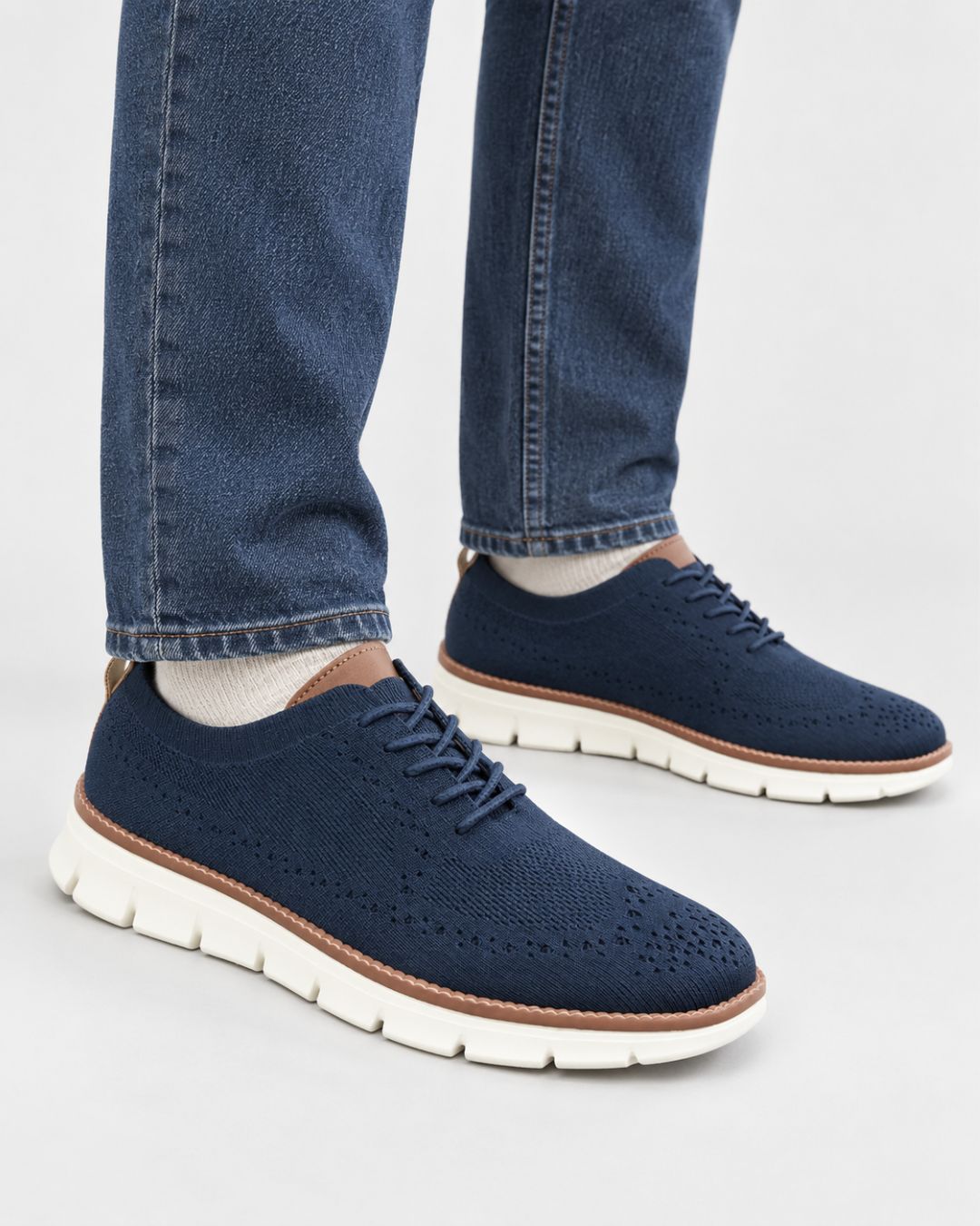 Men’s navy blue breathable mesh dress sneakers with brown trim and a white cushioned EVA sole worn with blue jeans.