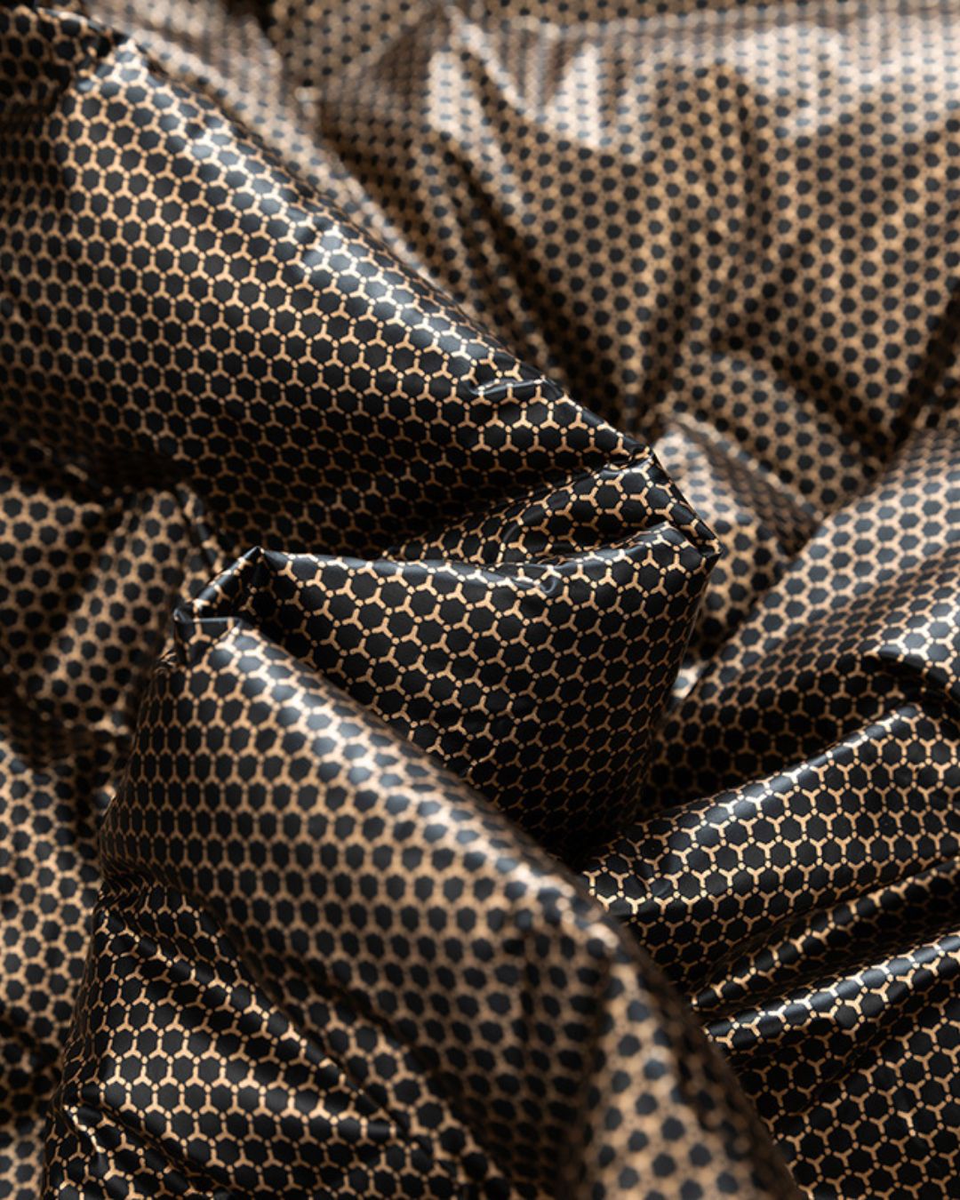Close-up of a black and gold honeycomb patterned fabric from a lightweight quilted down puffer jacket.