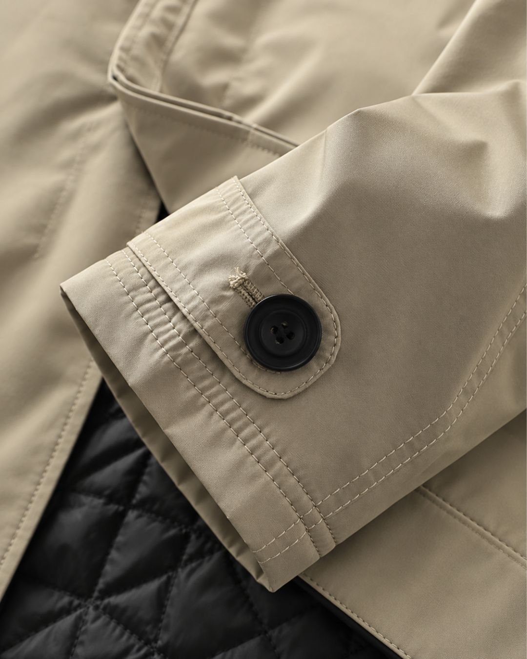 Beige men’s short trench coat sleeve with an adjustable button cuff and black quilted interior lining.