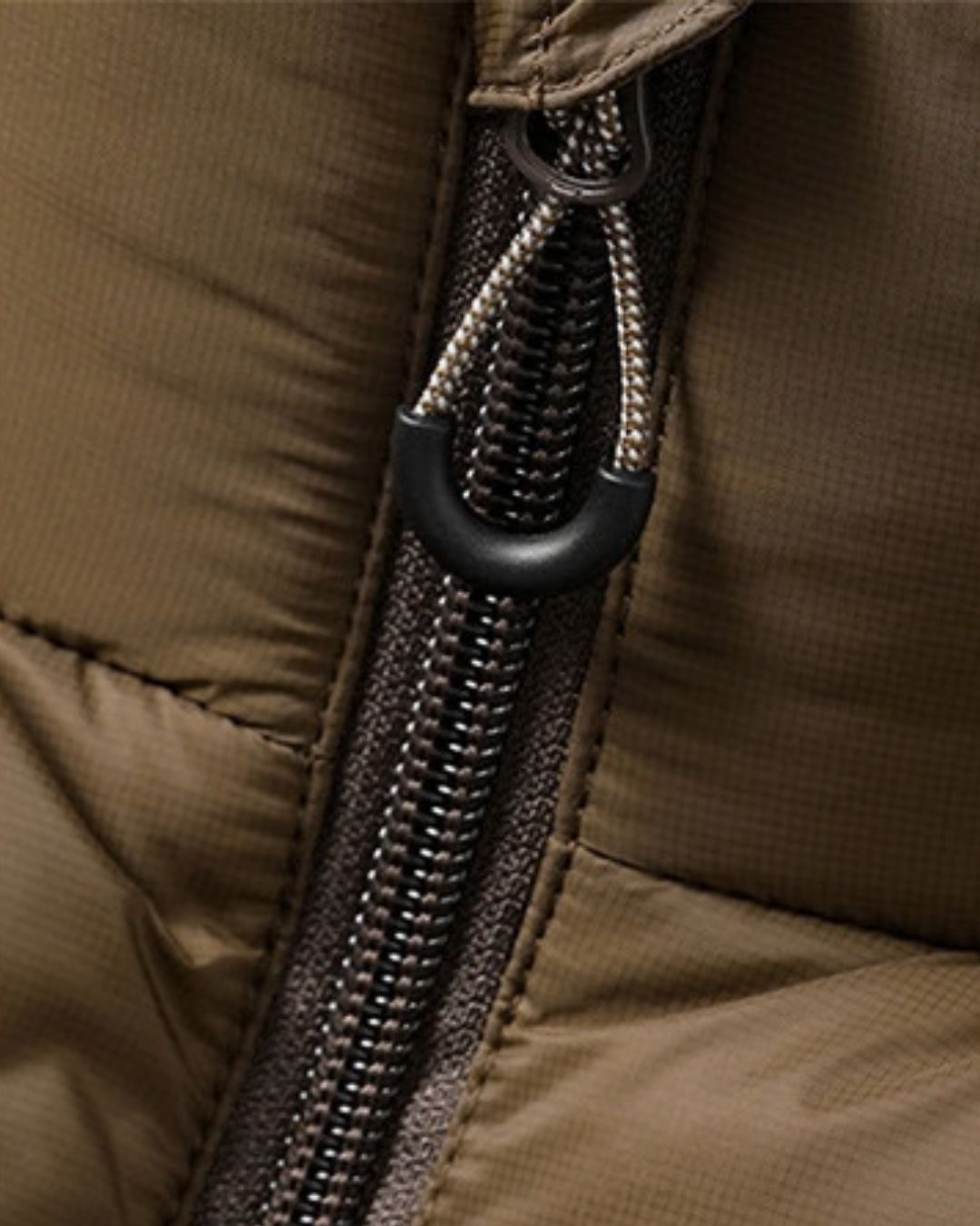 Close-up of a brown padded winter puffer jacket featuring a durable full-length zipper and a textured polyester fabric.