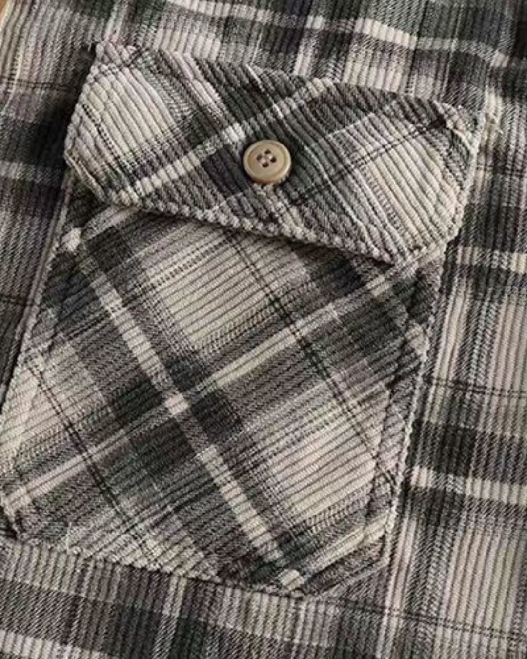 Close-up of a grey and white plaid corduroy shirt featuring a buttoned flap chest pocket and soft ribbed texture.