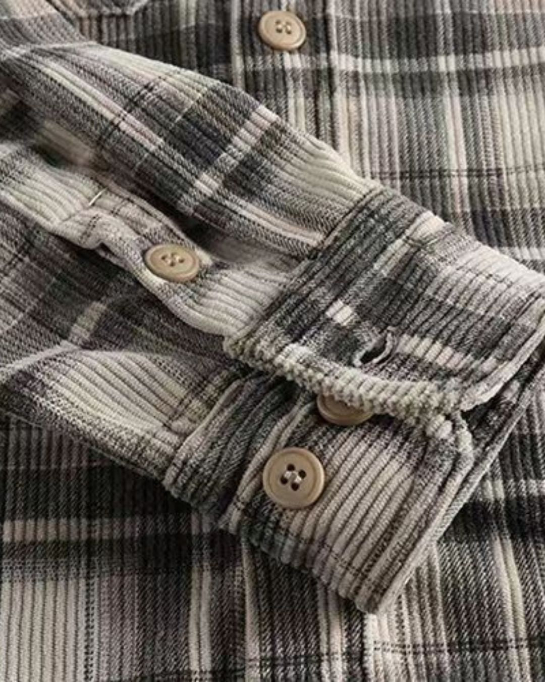Close-up of a grey and white plaid corduroy shirt featuring ribbed texture, long sleeves with buttoned cuffs, and a button-front.