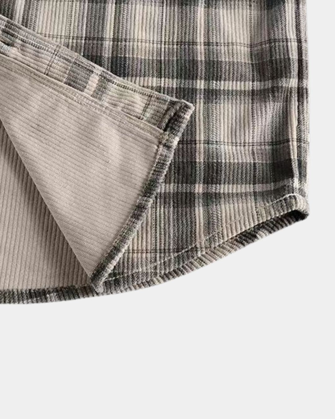 Close-up of a men’s grey and beige plaid corduroy shirt with a soft ribbed texture and curved hem.